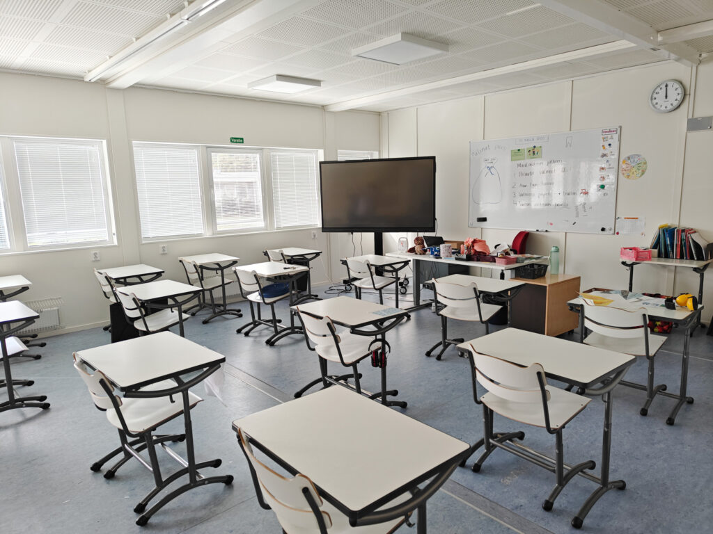 Valoisa luokkatila Herralan koulun väistötiloissa. Luokassa pulpetit on sijoiteltu väljästi niin, että niiden välissä mahtuu hyvin liikkumaan.